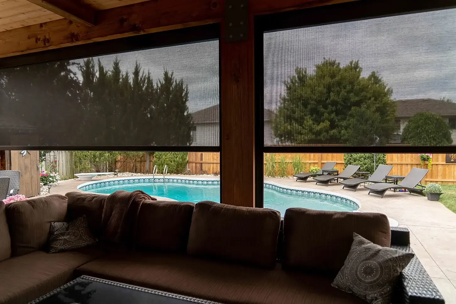 Backyard pool framed through a deployed solar mesh on a covered patio