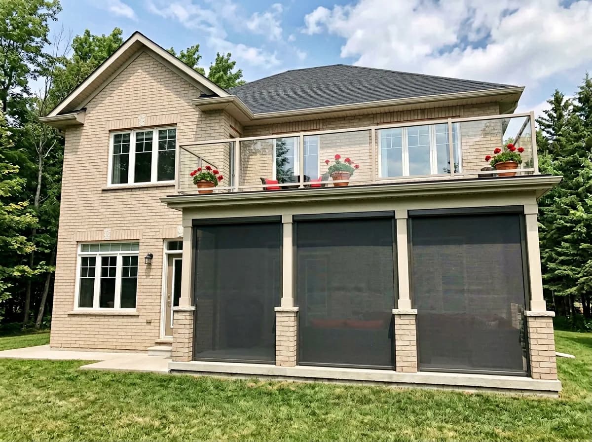 Multi-story Ontario home with glass-railed balcony and dark deployed retractable shades on the lower covered patio